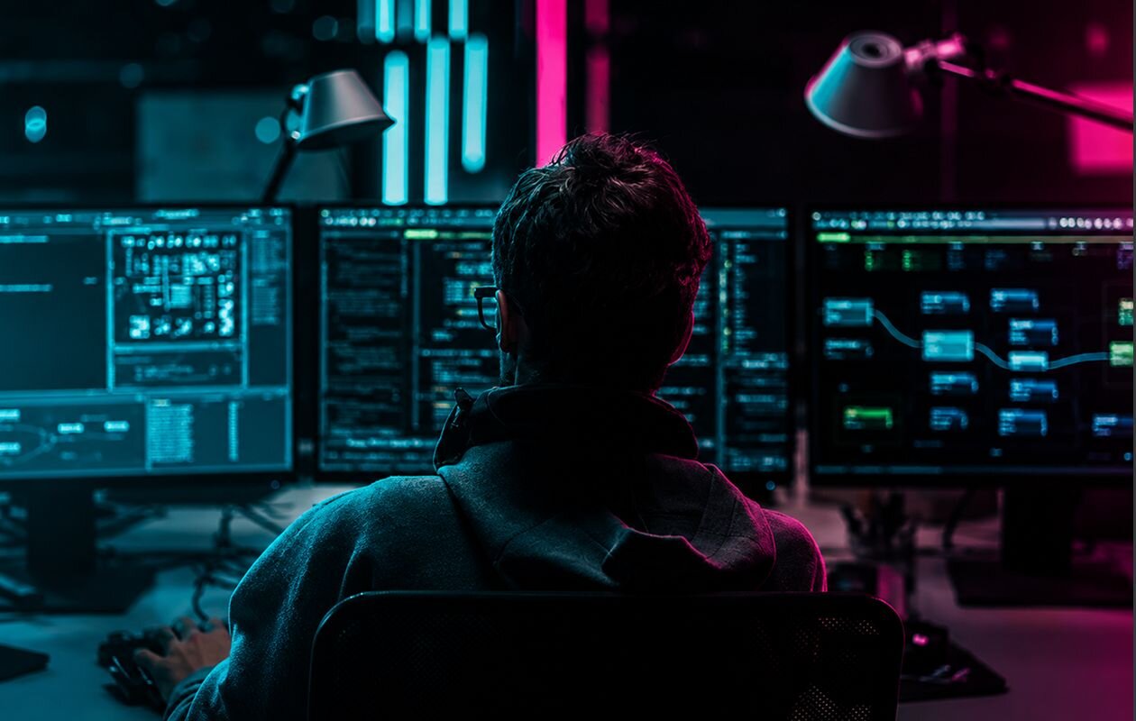 Man facing three computer monitors with code on them